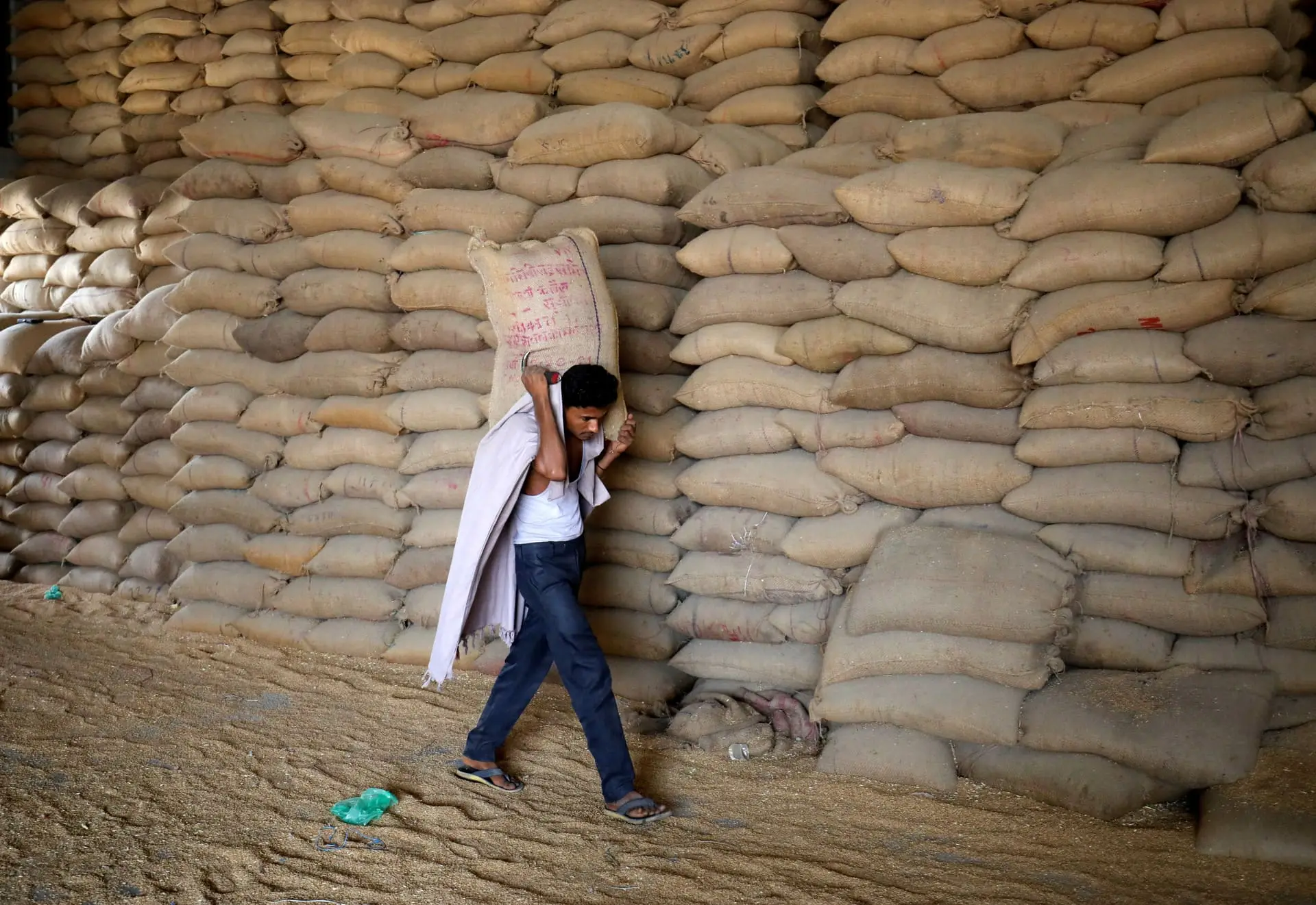 A worker carries a sack of wheat for sifting at a grain mill on the outskirts of Ahmedabad